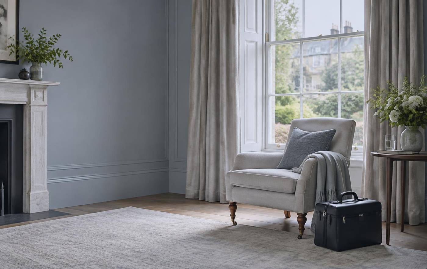 A quiet British sitting room with an armchair by a tall window and a clinical case beside it